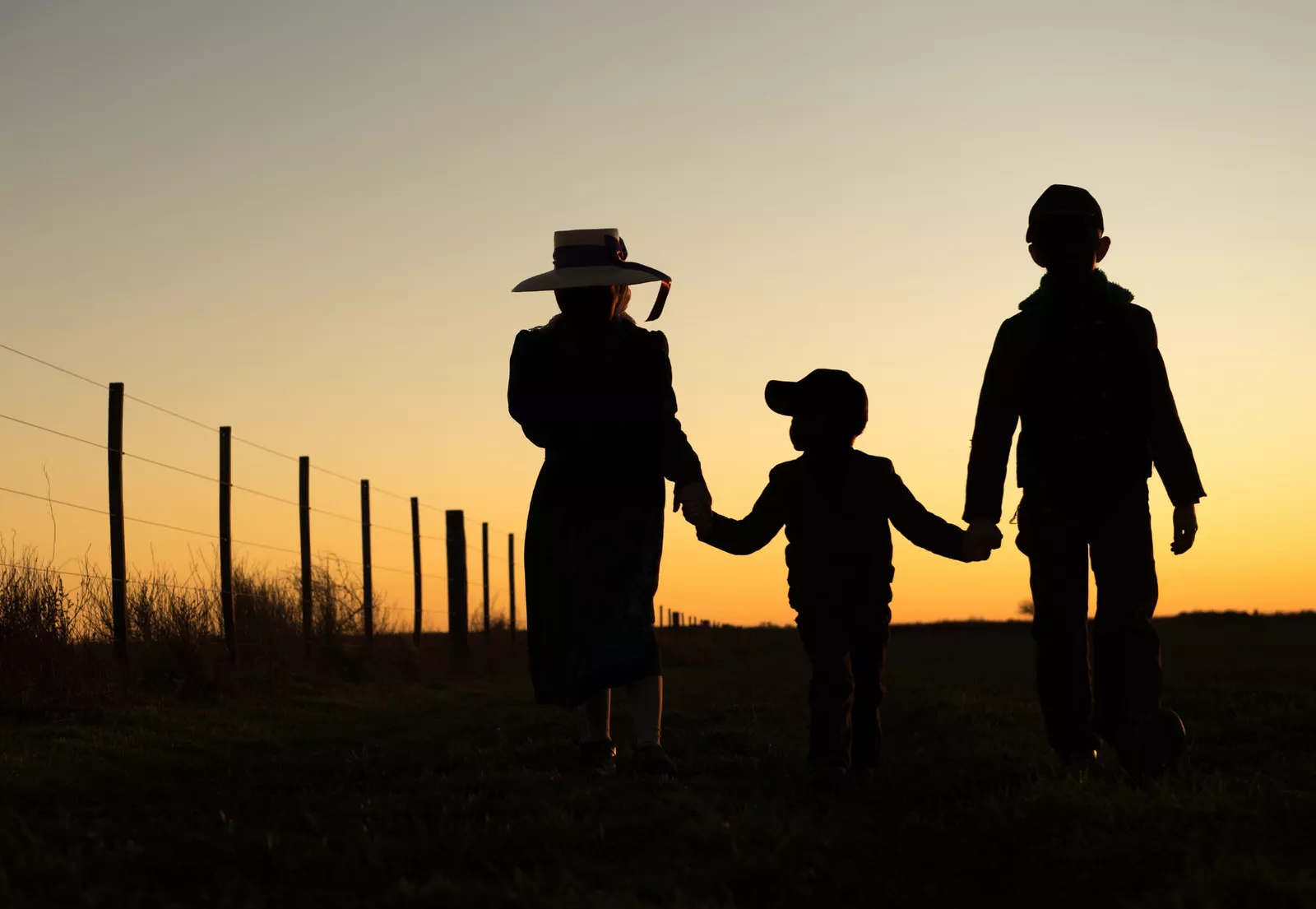 Three people taking a walk in a ranch at sunset.